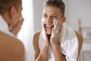 Photo of Man washing his face with cosmetic product near mirror in bathroom