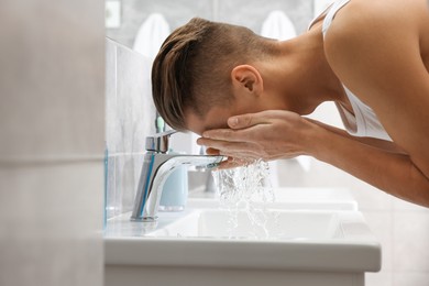 Photo of Man washing his face over sink in bathroom