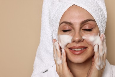 Photo of Beautiful woman washing her face with cleansing foam on beige background, space for text