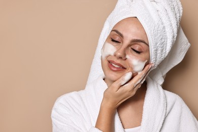 Photo of Beautiful woman washing her face with cleansing foam on beige background, space for text