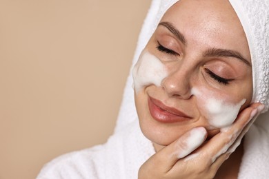 Photo of Beautiful woman washing her face with cleansing foam on beige background, space for text