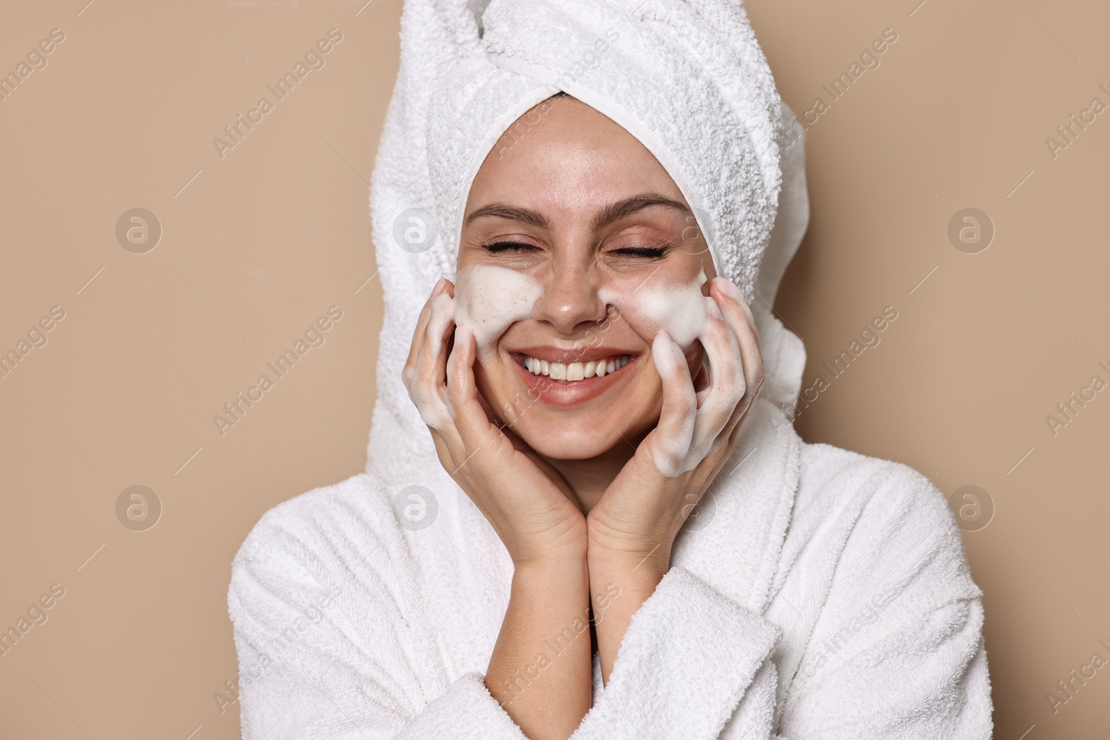 Photo of Beautiful woman washing her face with cleansing foam on beige background