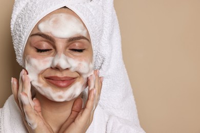 Photo of Beautiful woman washing her face with cleansing foam on beige background, space for text