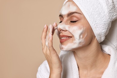 Photo of Beautiful woman washing her face with cleansing foam on beige background, space for text