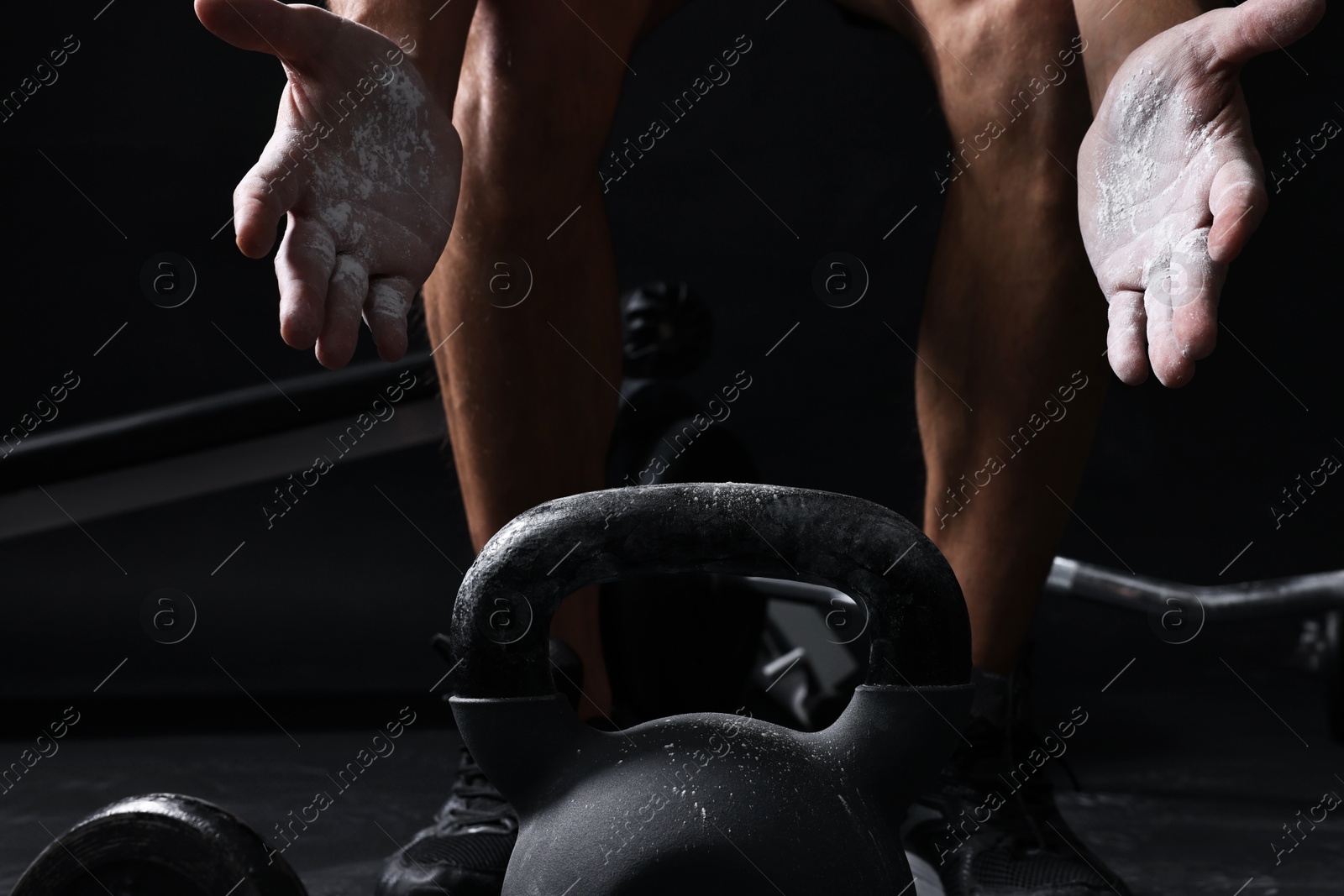 Photo of Man with talcum powder on hands training with kettlebell against black background, closeup