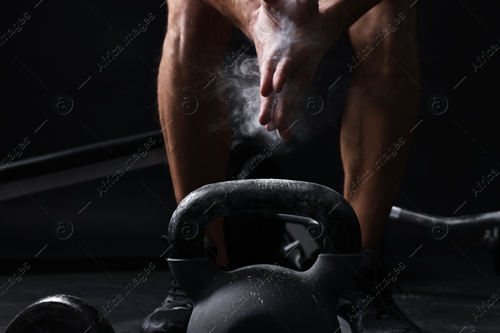 Photo of Man clapping hands with talcum powder before training with kettlebell on black background, closeup