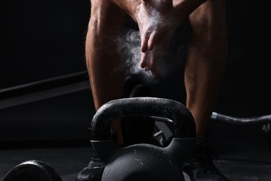 Photo of Man clapping hands with talcum powder before training with kettlebell on black background, closeup