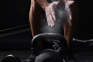 Photo of Man clapping hands with talcum powder before training with kettlebell on black background, closeup