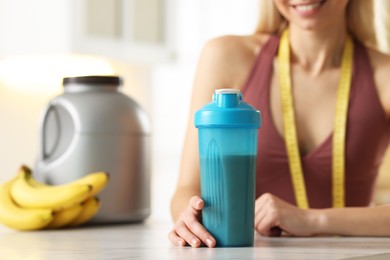 Photo of Weight loss. Woman with shaker of protein and measuring tape at white marble table in kitchen, closeup