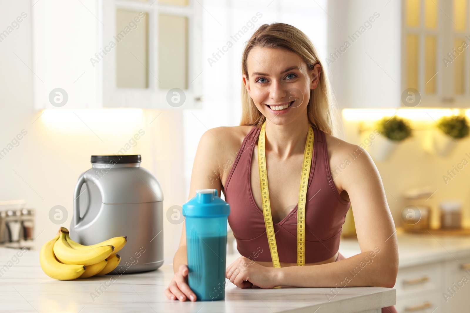 Photo of Weight loss. Woman with shaker of protein and measuring tape at white marble table in kitchen