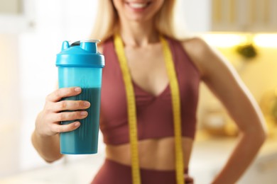 Photo of Weight loss. Woman with shaker of protein and measuring tape in kitchen, closeup