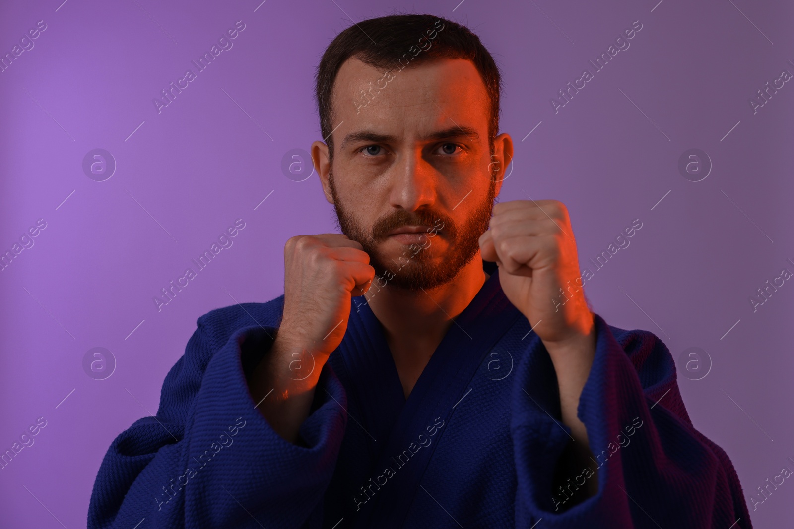 Photo of Karate fighter wearing uniform in color lights against violet background