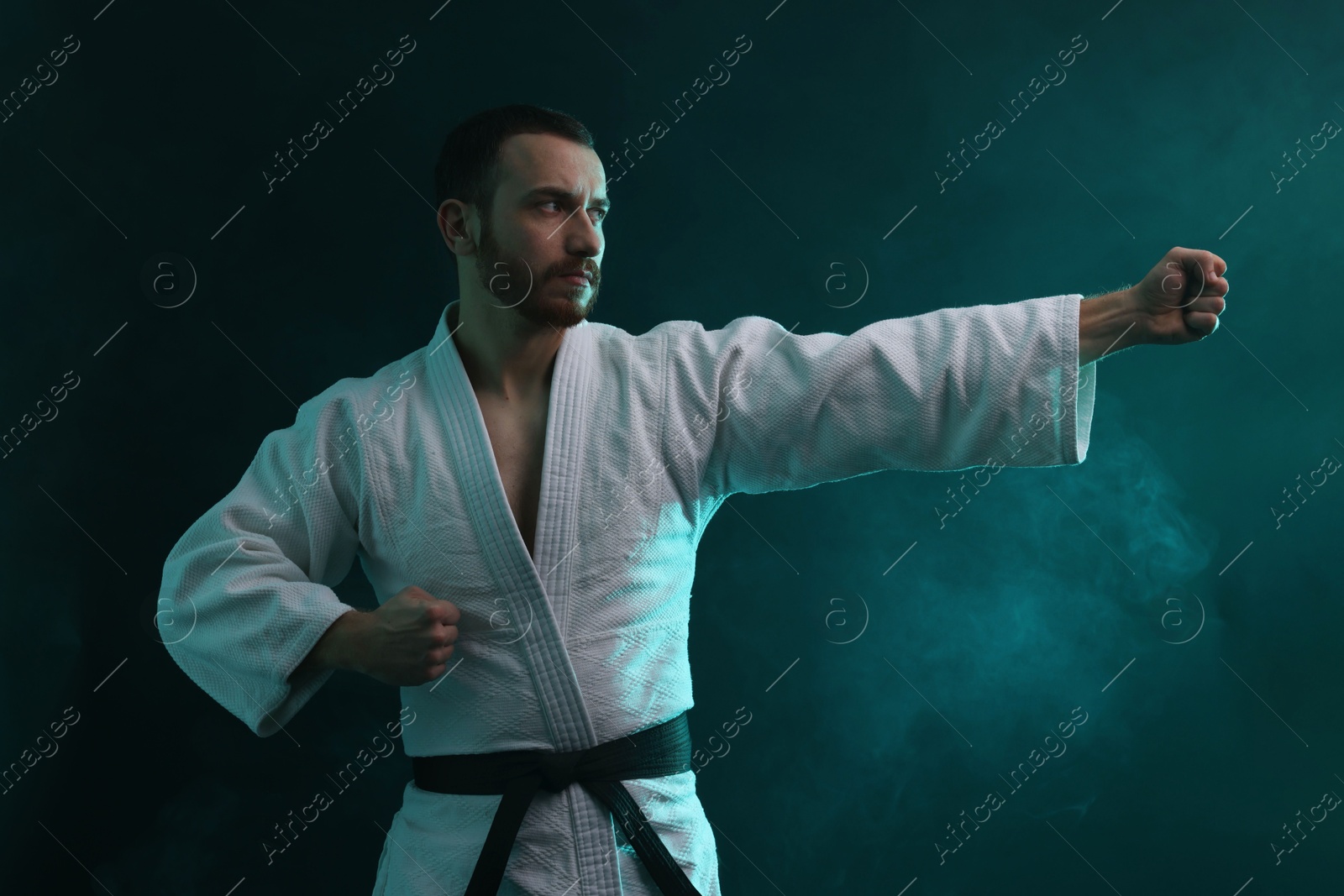 Photo of Man wearing uniform practicing karate in color lights and smoke