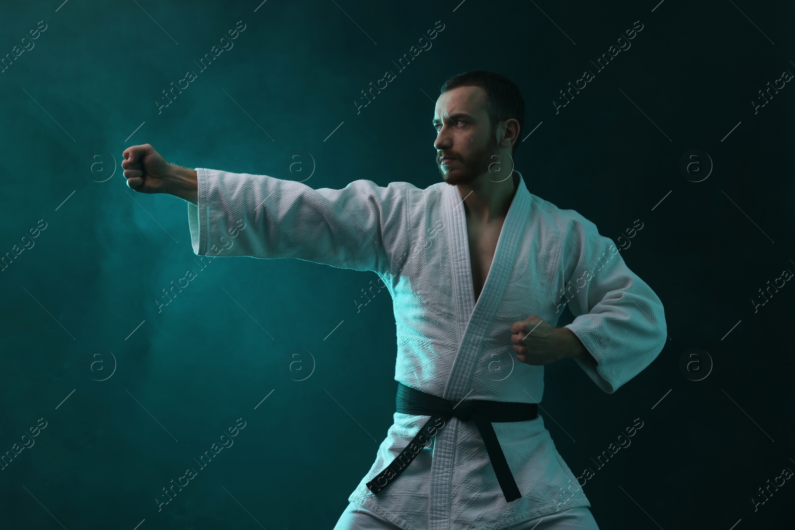 Photo of Man wearing uniform practicing karate in color lights and smoke