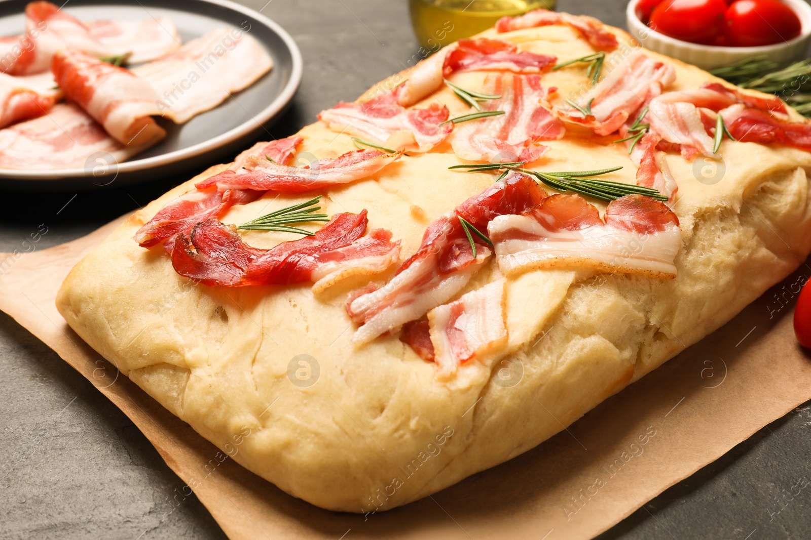 Photo of Delicious focaccia bread with bacon and rosemary on black table, closeup