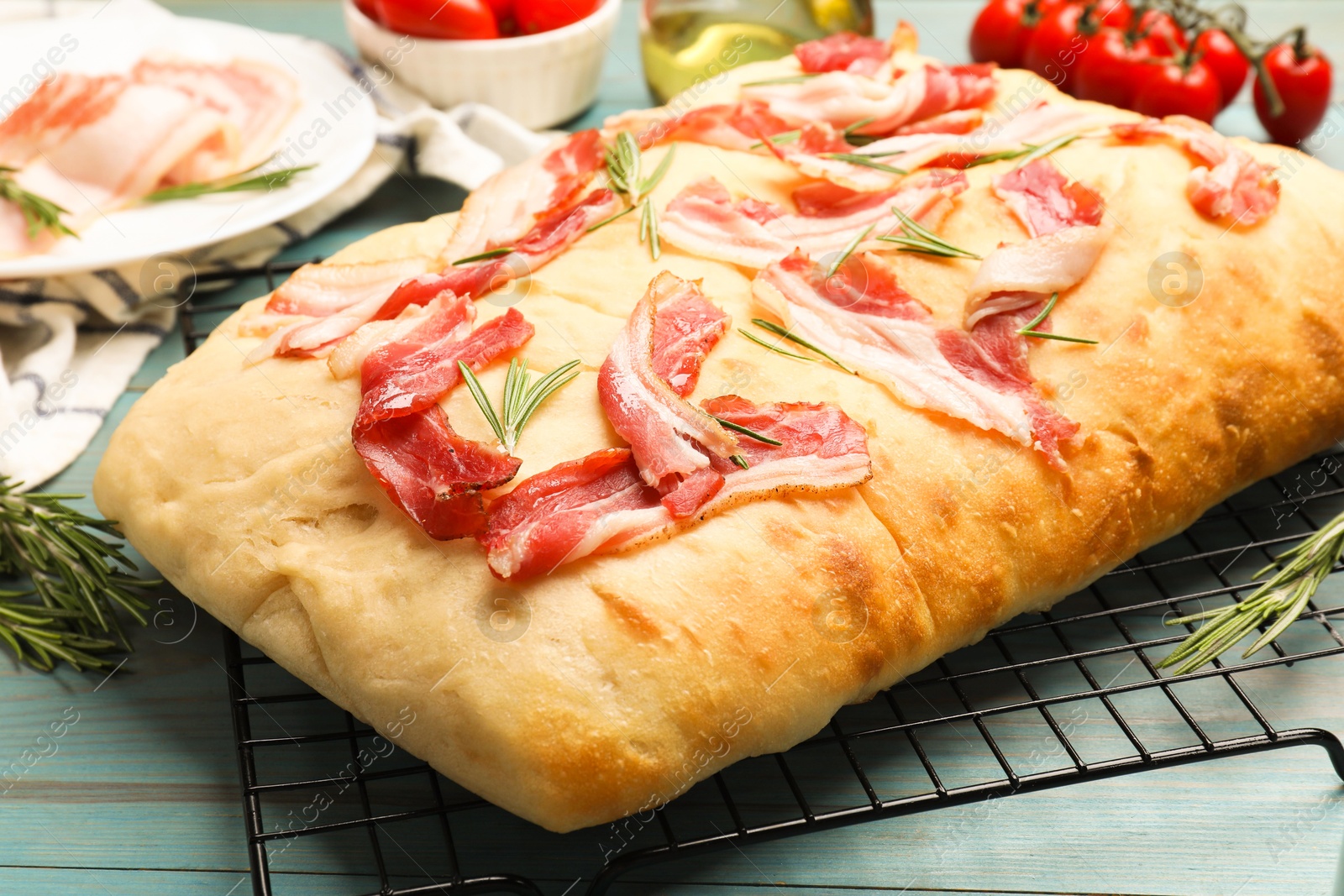 Photo of Delicious focaccia bread with bacon, rosemary and tomatoes on light blue wooden table, closeup