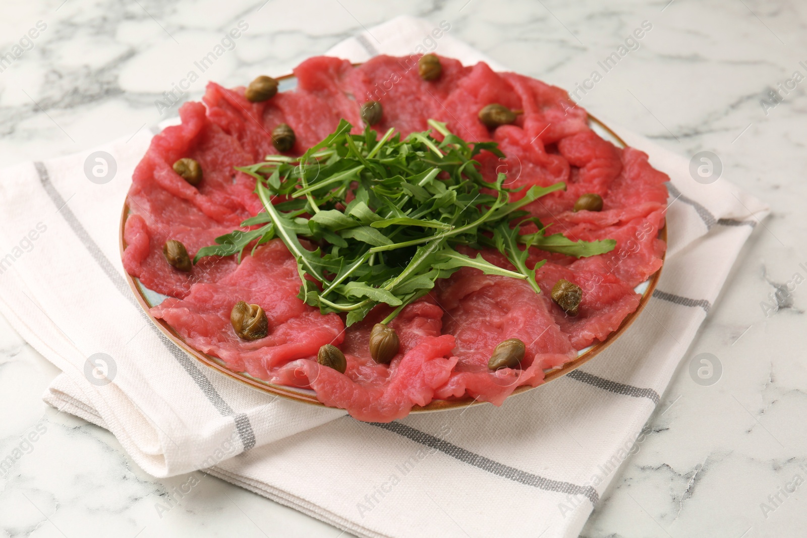 Photo of Delicious beef carpaccio with arugula and capers on white marble table, closeup