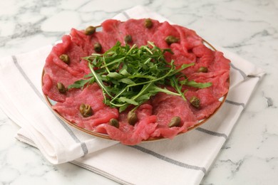 Delicious beef carpaccio with arugula and capers on white marble table, closeup