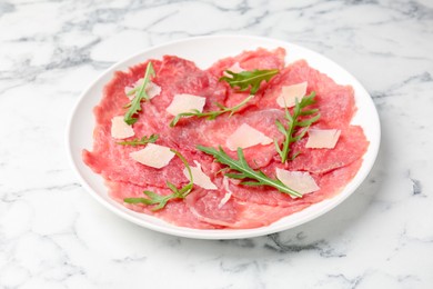 Delicious beef carpaccio with arugula and cheese on white marble table, closeup