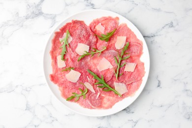 Photo of Delicious beef carpaccio with arugula and cheese on white marble table, top view