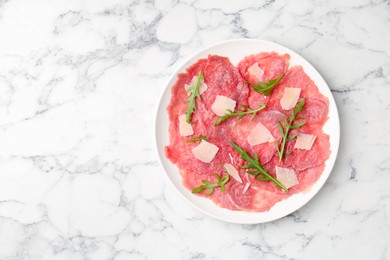 Delicious beef carpaccio with arugula and cheese on white marble table, top view. Space for text