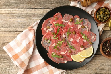 Photo of Delicious beef carpaccio with arugula, capers, cheese and lemon on wooden table, flat lay