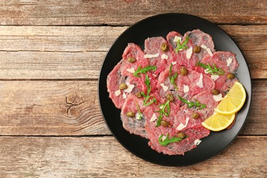 Photo of Delicious beef carpaccio with arugula, capers, cheese and lemon on wooden table, top view. Space for text