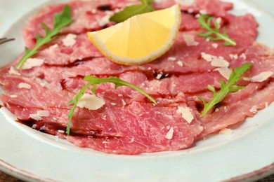 Delicious beef carpaccio with arugula, cheese, balsamic vinegar and lemon on plate, closeup