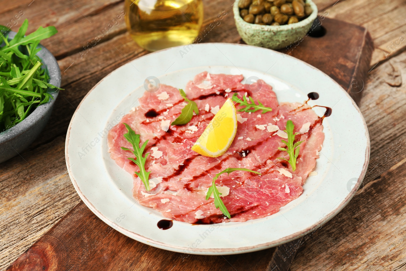 Photo of Delicious beef carpaccio with arugula, cheese, balsamic vinegar and lemon on wooden table, closeup