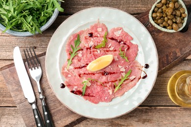 Delicious beef carpaccio served on wooden table, flat lay