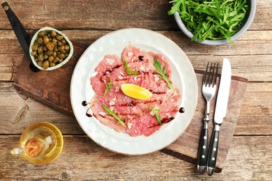 Delicious beef carpaccio served on wooden table, flat lay