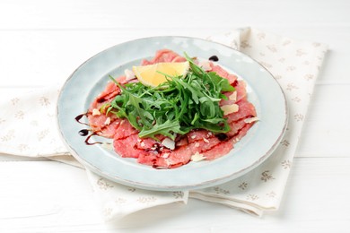 Photo of Delicious beef carpaccio with arugula, cheese, balsamic vinegar and lemon on white wooden table, closeup