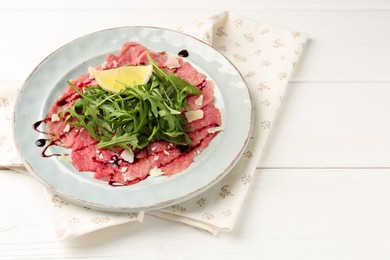 Delicious beef carpaccio with arugula, cheese, balsamic vinegar and lemon on white wooden table, closeup. Space for text