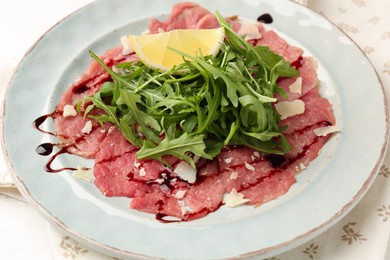 Delicious beef carpaccio with arugula, cheese, balsamic vinegar and lemon on table, closeup