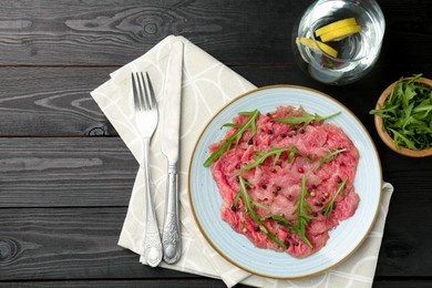 Photo of Fresh beef carpaccio with arugula and peppercorns served on black wooden table, flat lay. Space for text