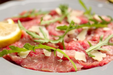 Photo of Fresh beef carpaccio with arugula, cheese and lemon on plate, closeup