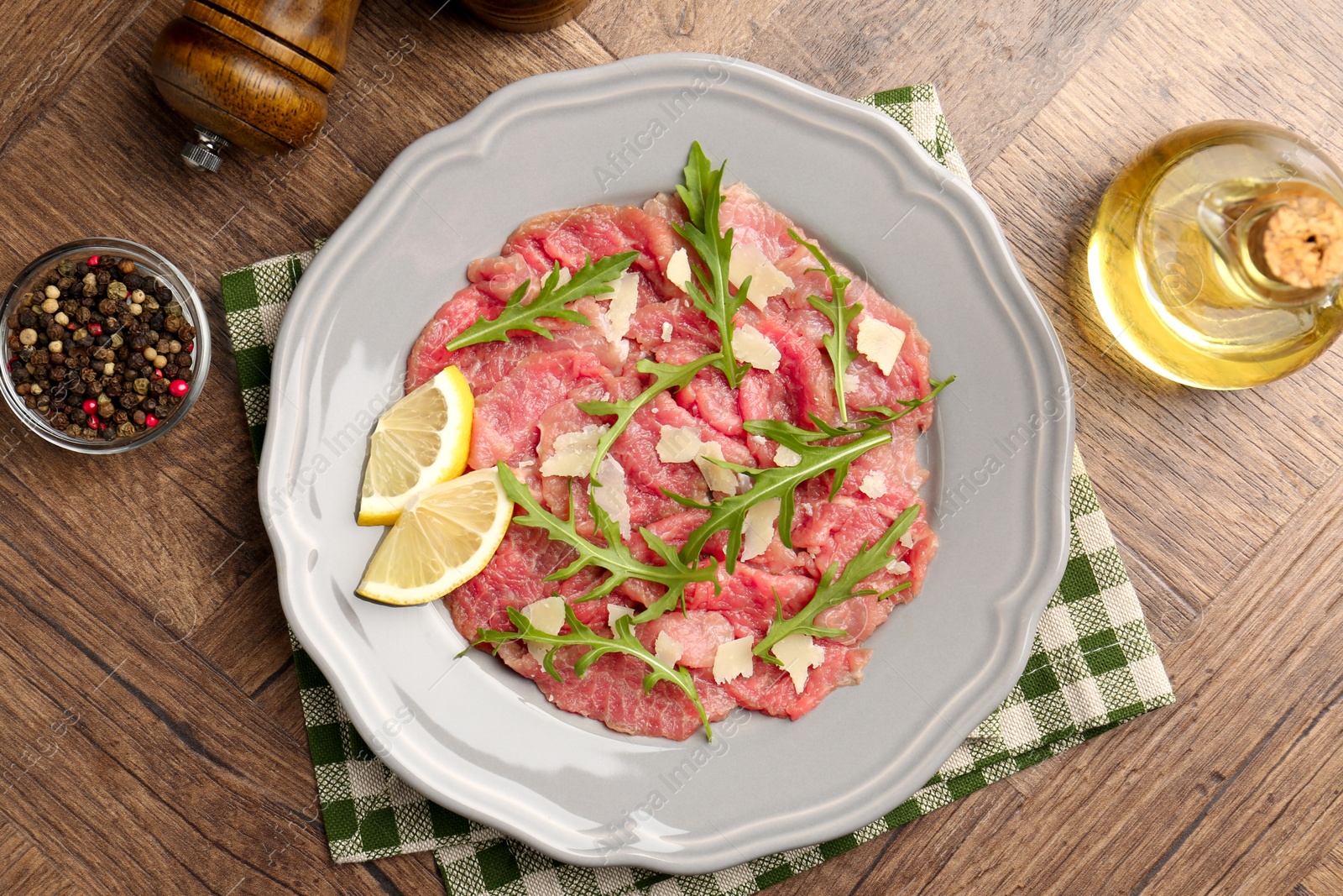 Photo of Fresh beef carpaccio with arugula, cheese and lemon on wooden table, flat lay