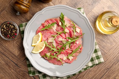 Fresh beef carpaccio with arugula, cheese and lemon on wooden table, flat lay