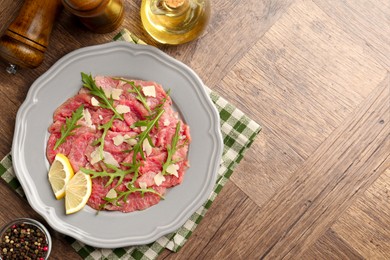 Fresh beef carpaccio with arugula, cheese and lemon on wooden table, flat lay. Space for text