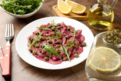 Photo of Fresh beef carpaccio with arugula and capers on wooden table, closeup