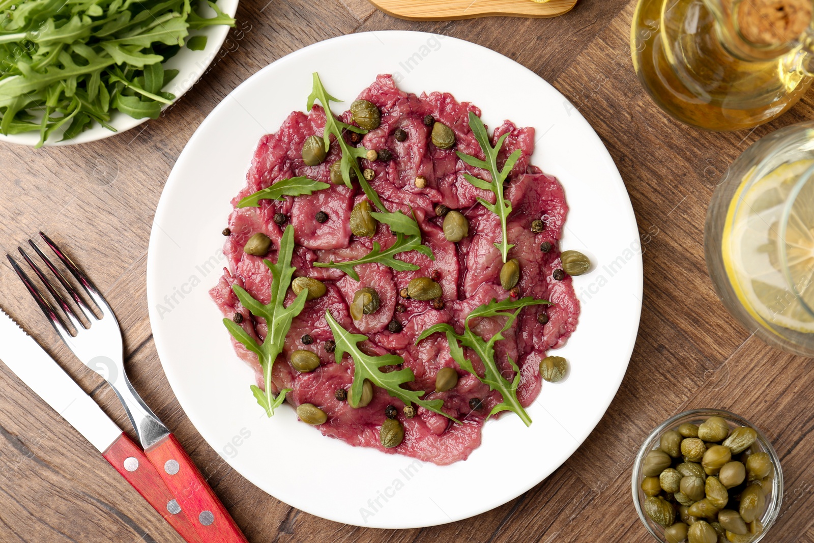 Photo of Fresh beef carpaccio with arugula and capers served on wooden table, flat lay