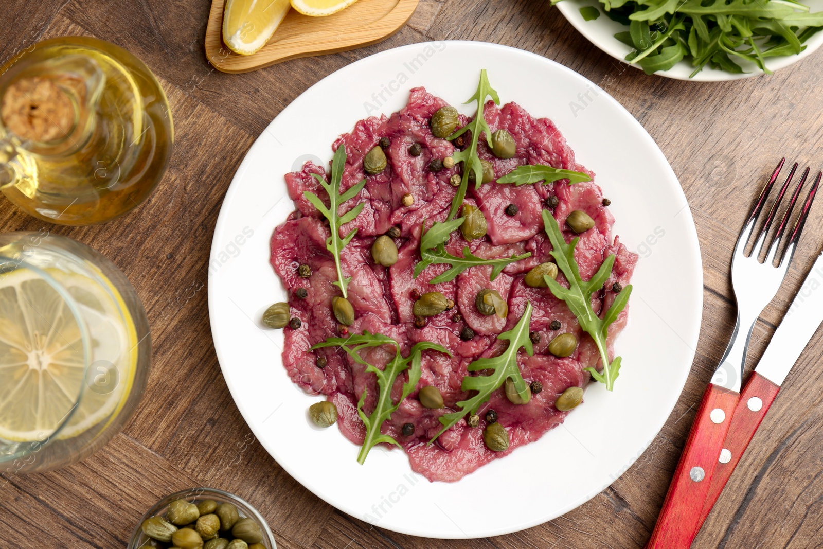 Photo of Fresh beef carpaccio with arugula and capers served on wooden table, flat lay