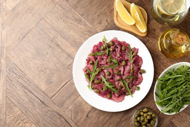 Fresh beef carpaccio with arugula and capers on wooden table, flat lay. Space for text