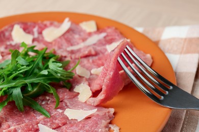 Photo of Eating fresh beef carpaccio with arugula and cheese on beige table, closeup