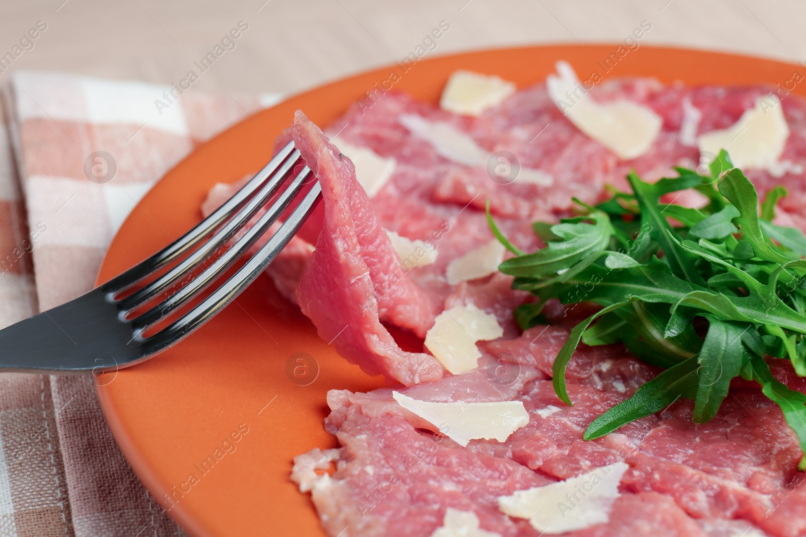 Photo of Eating fresh beef carpaccio with arugula and cheese on beige table, closeup