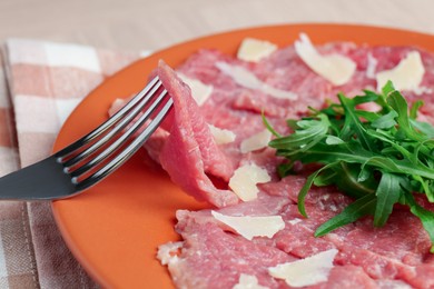 Photo of Eating fresh beef carpaccio with arugula and cheese on beige table, closeup