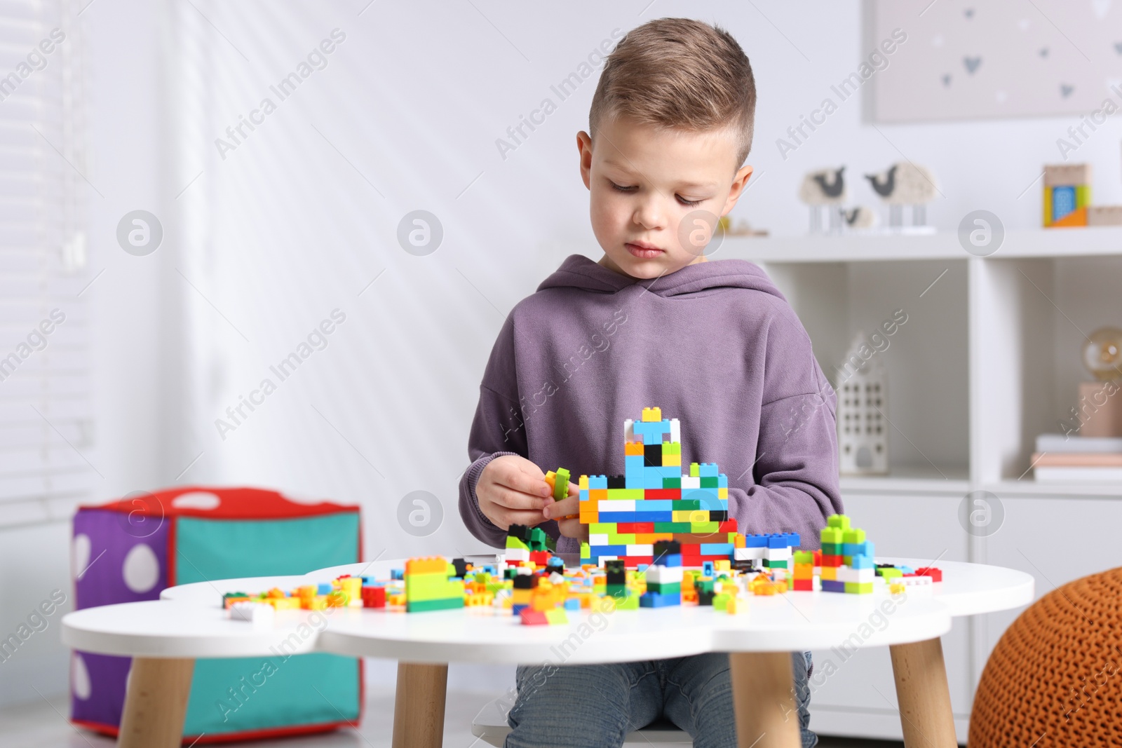 Photo of Cute boy playing with building blocks at white table indoors