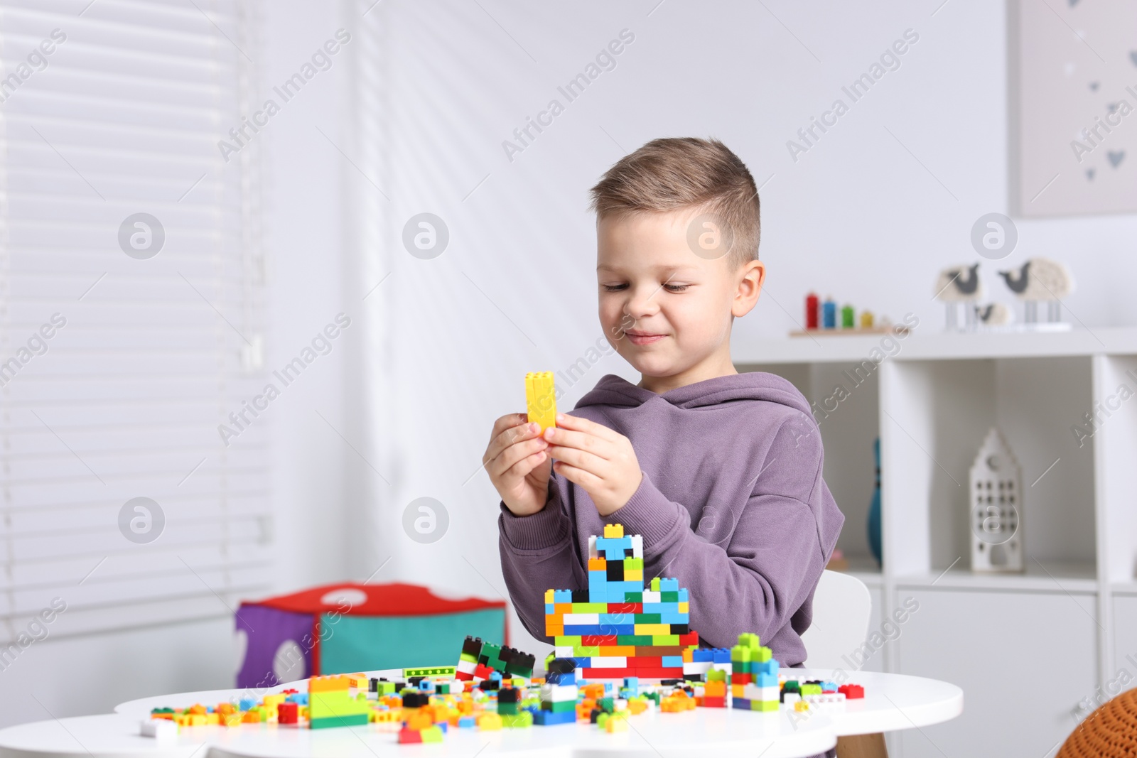 Photo of Cute boy playing with building blocks at white table indoors