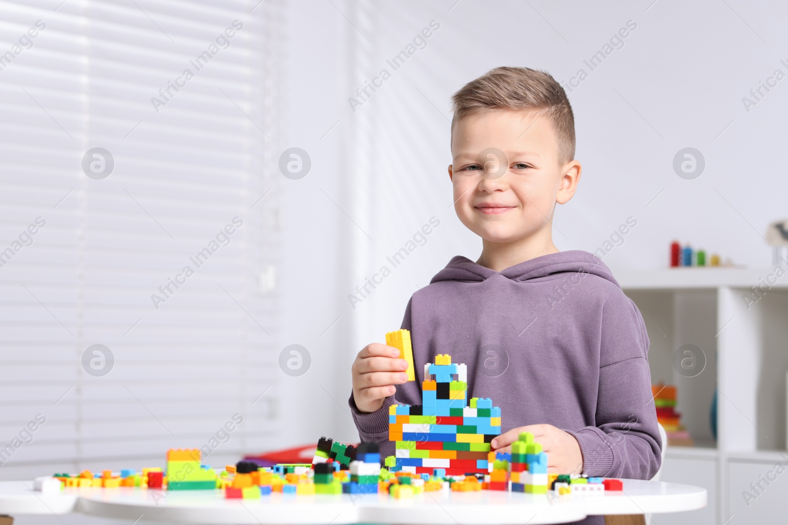 Photo of Cute boy playing with building blocks at white table indoors. Space for text