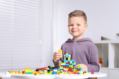 Photo of Cute boy playing with building blocks at white table indoors. Space for text